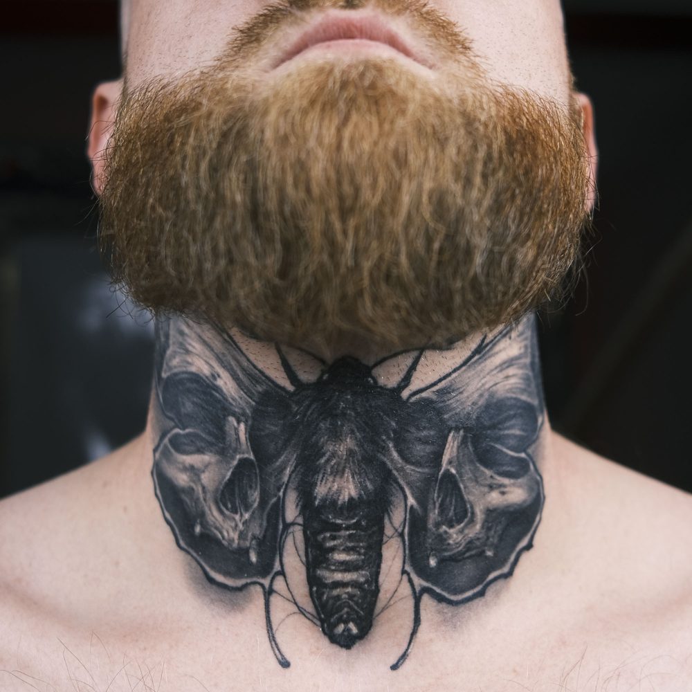 picture of neck tattoo featuring a black and grey moth with skull wings