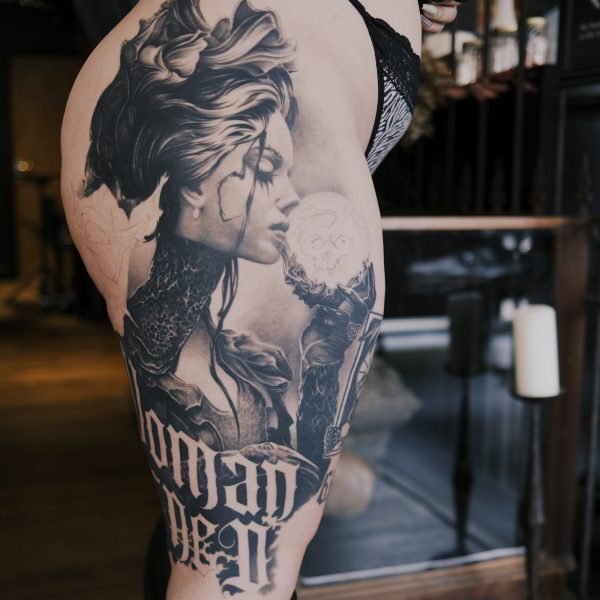 image of the side of a womans thigh with large black and grey tattoo of a victorian lady holding a crystal ball