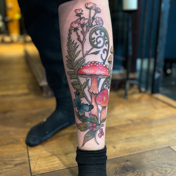 image of a leg tattoo which features mushrooms, foxglove flowers, twirling leaves and vines all done in bright colours.