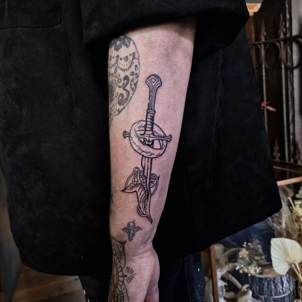 image of an arm tattoo featuring the shards of narsil sword and elven leaf brooch from lord of the rings