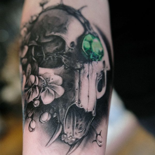 image of a tattoo featuring a cat skull, flowers and green jewel in the middle of the cat skull forehead all done in a soft black and grey style