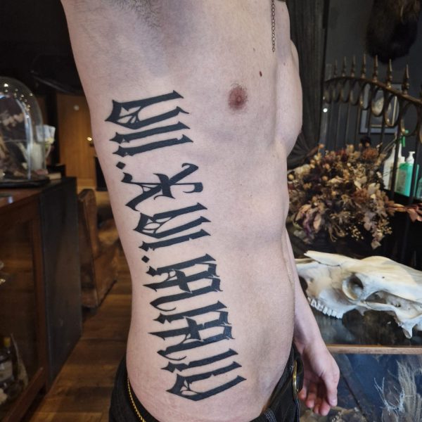 Image of a bare torso standing to the side showing a huge letting tattoo down the ribs