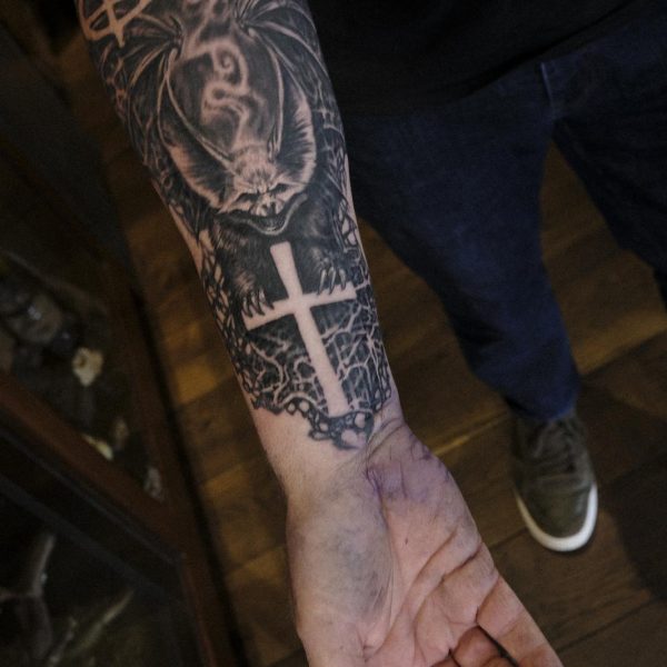 Ozzy tattoo with bat, lettering and cross on wrist and upper arm