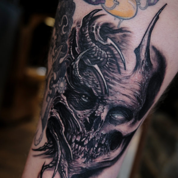 Photo of two tattoos on a leg. Top tattoo is a rubber duck ball gag and the lower is a morph skull tattoo