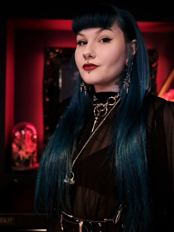 Sarah-Jemimah-Portrait Image showing a headshot of tattoo artist Sarah Jemimah who has long blue hair and full fringe wearing black with silver jewellery