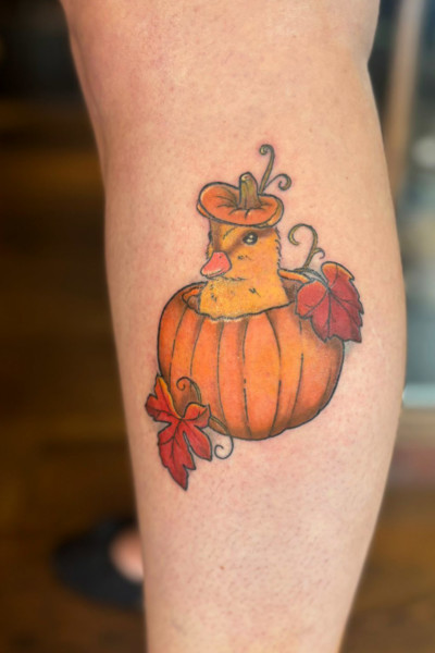 image of a tattoo of a cute duckling poking it's head out of a pumpkin with leaves either side.