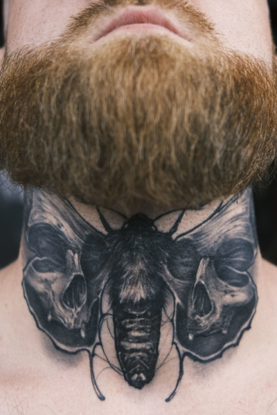 picture of neck tattoo featuring a black and grey moth with skull wings