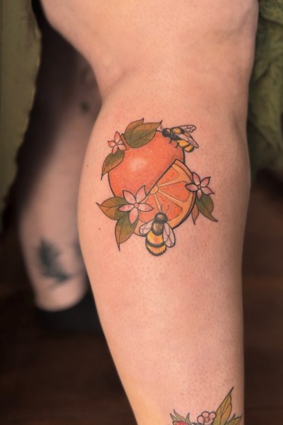 image of a leg tattoo featuring an orange and bees with flowers in a colour whimsical style