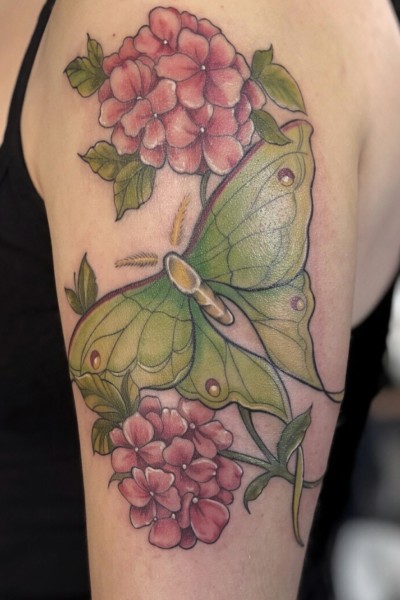 close up image of an arm tattoo of a beautiful large green lunar moth with pink flowers either side