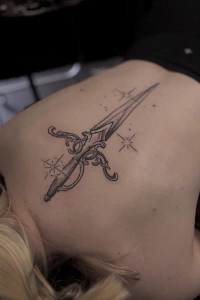An image of a womans back featuring a ornate dagger tattoo
